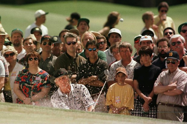 Greg Norman chips out of the bunker and onto the green on the first hole.